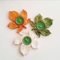 two green candles are sitting next to each other on a white surface with leaves around them