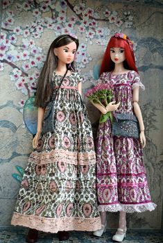 two dolls standing next to each other in front of a wall with flowers on it