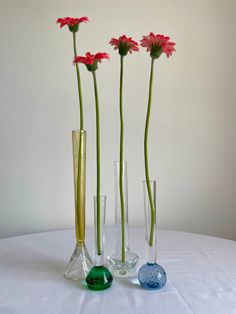 three vases with flowers in them sitting on a white table cloth covered tablecloth