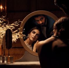 a man and woman looking at each other in front of a mirror with flowers on it