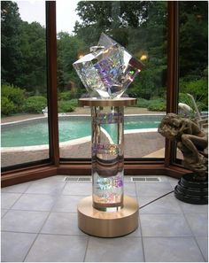 a glass vase sitting on top of a wooden stand in front of a large window