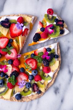 a fruit pizza is cut into slices on a marble counter top with berries, kiwis and blueberries