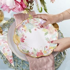 a person is setting a plate on a table with napkins and flowers in the background