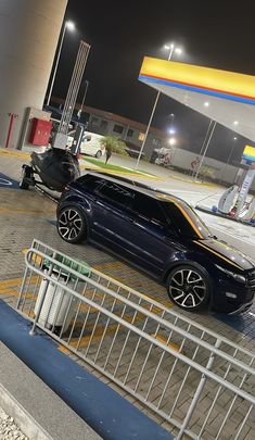 two cars are parked in front of a gas station at night, one is blue and the other is black