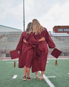 two women in red graduation gowns standing on a football field with their arms around each other