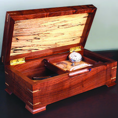 an open wooden box with a watch and other items in it on top of a table