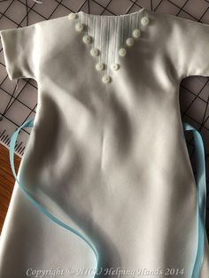 a baby's dress made out of white and blue material with pearls on the collar