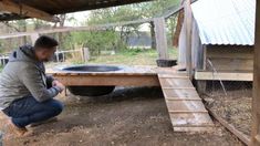 a man kneeling down in front of a chicken coop and looking at something on the ground