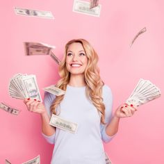 a woman holding money in her hands while standing against a pink background with falling bills