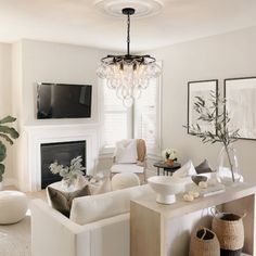 a living room filled with white furniture and a chandelier hanging from the ceiling