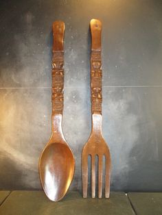 two wooden utensils are sitting next to each other on a table with a gray wall in the background