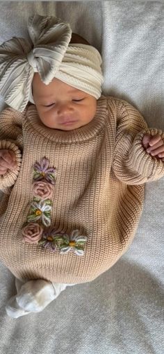 a baby is laying down wearing a sweater and headband