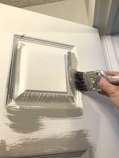 a person holding a paintbrush in front of a white door with a square frame painted on it