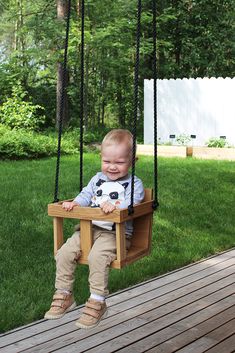 a baby sitting in a wooden swing with a soccer ball on it's chest