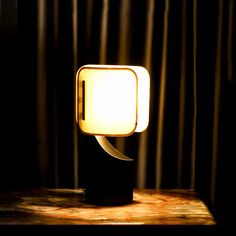 a table lamp sitting on top of a wooden table next to a curtained window