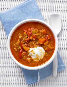 a white bowl filled with soup on top of a blue and white table cloth next to a spoon