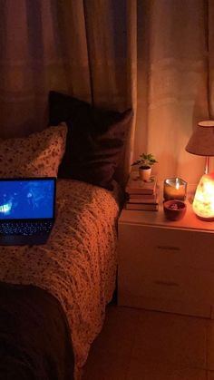 a laptop computer sitting on top of a bed next to a night stand and lamp