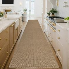 a long kitchen with white cabinets and beige rugs on the floor in front of an oven