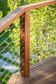 a close up of a wooden railing on a deck with green trees in the background