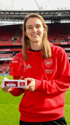 a female soccer player holding a trophy in front of an empty football stadium with fans