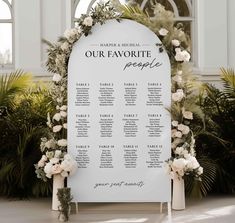 a white wedding seating sign with flowers and greenery on the side for an outdoor ceremony