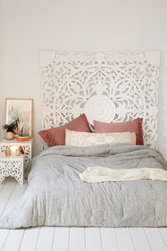 a bedroom with a white headboard and grey bedspread, pink pillows and pictures on the wall