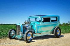 an old blue car parked on the side of a dirt road