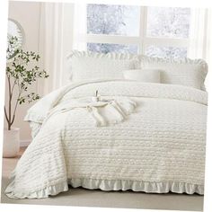 a white comforter with ruffles and pillows in front of a large window