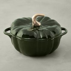 a green pot with a gold handle on the top, sitting in front of a gray background