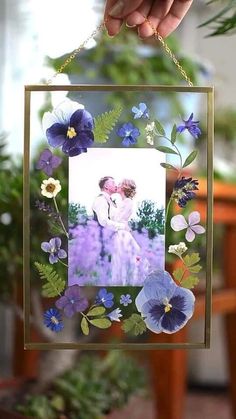 a person holding up a photo frame with flowers on the front and side, hanging from a chain