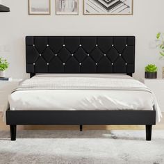 a bed with black headboard and foot board in a white room next to potted plants