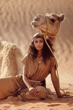 a woman sitting on the ground next to a camel