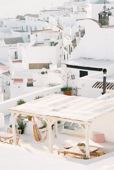 an outdoor table and chairs on the roof of a white building with lots of buildings in the background