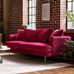 a living room with brick walls and red couches in front of a window that has potted plants on it