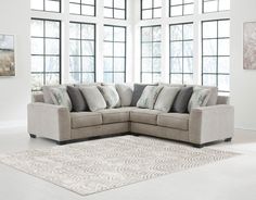 a large sectional couch with pillows on it in front of two windows and a rug