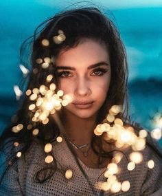 a woman standing in front of the ocean with her eyes closed and lights coming out