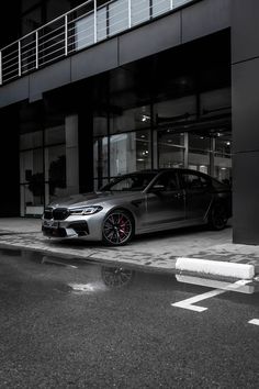 a silver car parked in front of a tall building next to a white cross walk