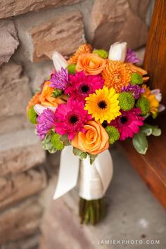 a bouquet of colorful flowers sitting on top of a wooden bench next to a stone wall