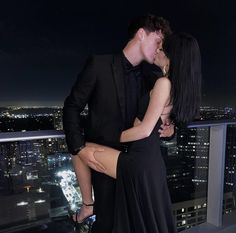 a man and woman kissing in front of a cityscape at night with lights on