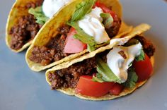 three tacos on a plate with sour cream and tomatoes