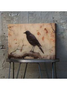 a black bird sitting on top of a metal stool next to a wall with leaves