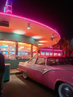 a pink car parked in front of a fast food restaurant with neon lights on the roof