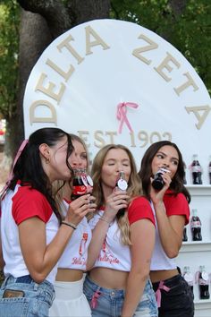 three girls are standing in front of a sign and one girl is holding a cell phone