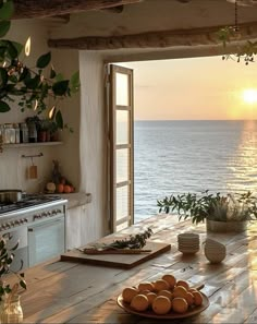 a kitchen with an open window overlooking the ocean and sun rising over the water in the distance