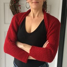 a woman with her arms crossed standing in front of a door wearing a red cardigan