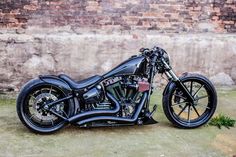 a black motorcycle parked in front of a brick wall with grass growing on the ground