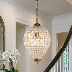 a chandelier hanging from the ceiling in a foyer with white flowers and greenery