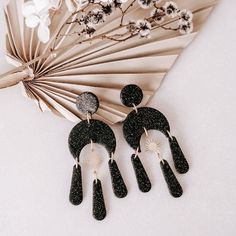 two black and white earrings sitting on top of a table next to a flower arrangement