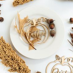 a white plate topped with an acorn and wooden name cutout next to fall decorations