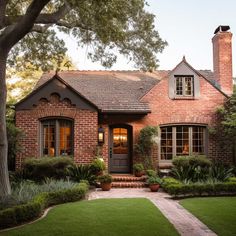 a brick house with lots of windows and plants in front of the door is surrounded by greenery